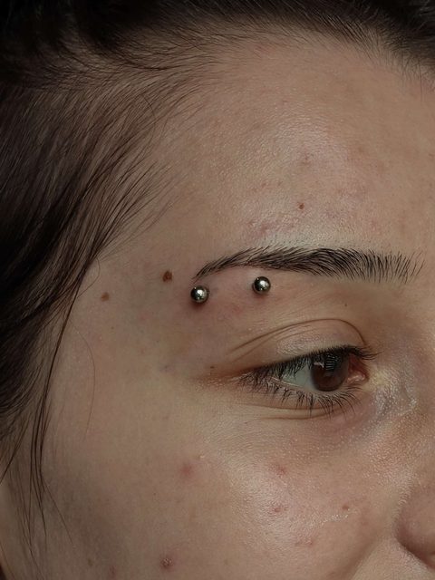 Eyebrow piercing with two small silver balls above the eye