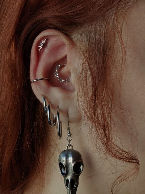Ear with a crystal helix stud, conch ring and a bird-skull drop on the lobe