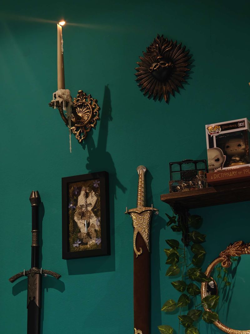 A lit candle in a brass sconce, a black sacred-heart sunburst and two swords on the studio wall