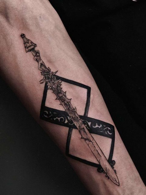 Forearm tattoo of a long ornate spear crossing a bold black rune band