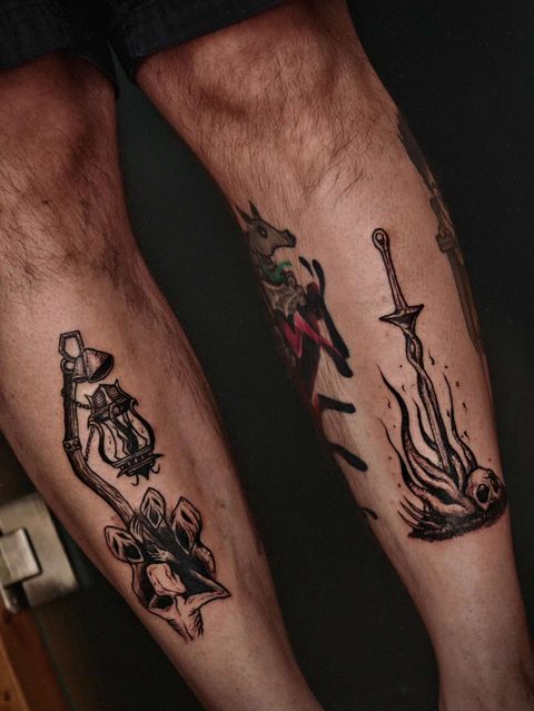 Several small black tattoos on a pair of calves: a lantern key, a sword and a burning flame