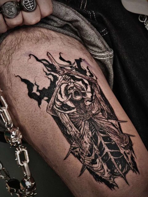 Thigh tattoo of a hooded skeletal figure in tattered robes, framed by black flame shapes