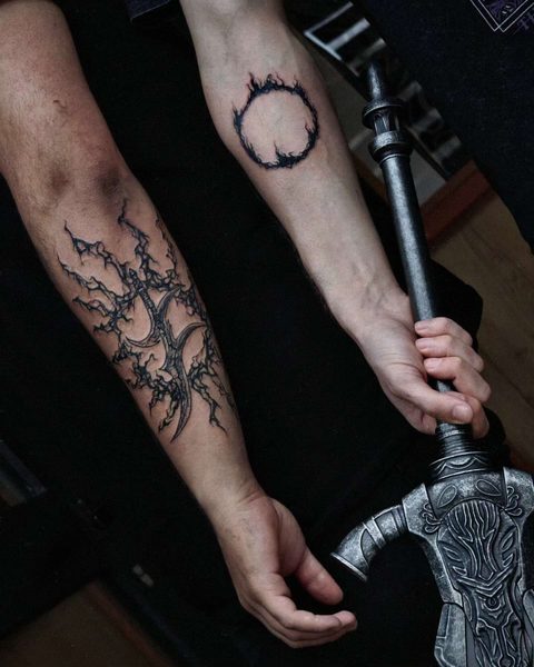 Forearm tattoos of a branching black sigil and a small burning ring