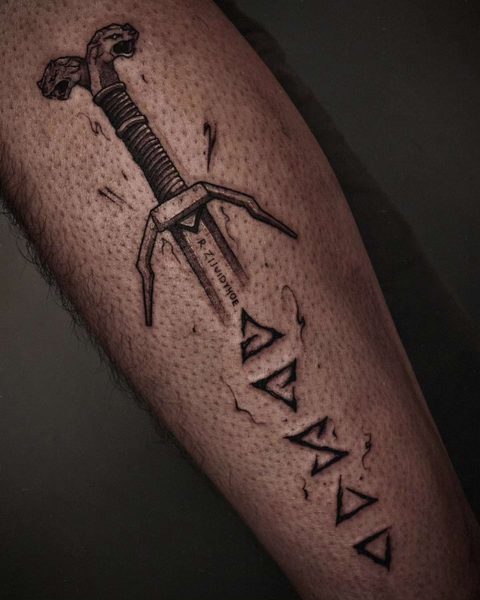 Calf tattoo of a forked dagger above a column of five rune-like signs