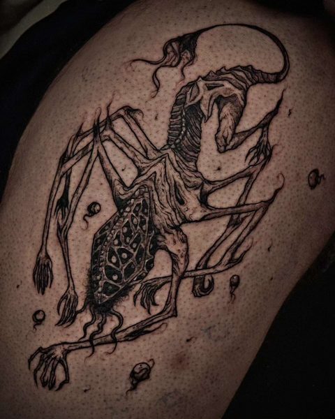 Thigh tattoo of a gaunt skeletal creature with long limbs and a ribbed body